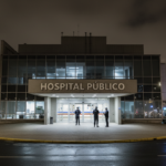 Fachada de um hospital público à noite, com iluminação de segurança.