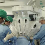 Braço robótico cirúrgico sendo controlado remotamente por médicos em uma sala de cirurgia avançada.