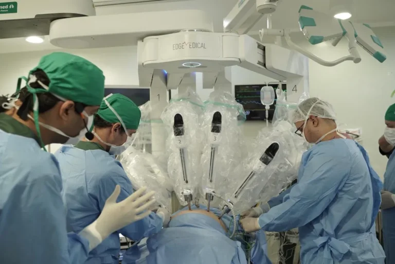 Braço robótico cirúrgico sendo controlado remotamente por médicos em uma sala de cirurgia avançada.