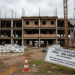 Escola em construção paralisada em João Pessoa, com materiais de construção expostos.