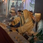 Encenação da Paixão de Cristo em bairro popular de João Pessoa com atores e público envolvido na cena.