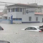 Rua alagada em cidade brasileira durante forte tempestade com chuva intensa e vento.