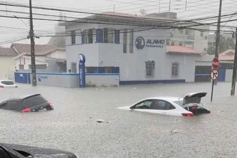 Rua alagada em cidade brasileira durante forte tempestade com chuva intensa e vento.
