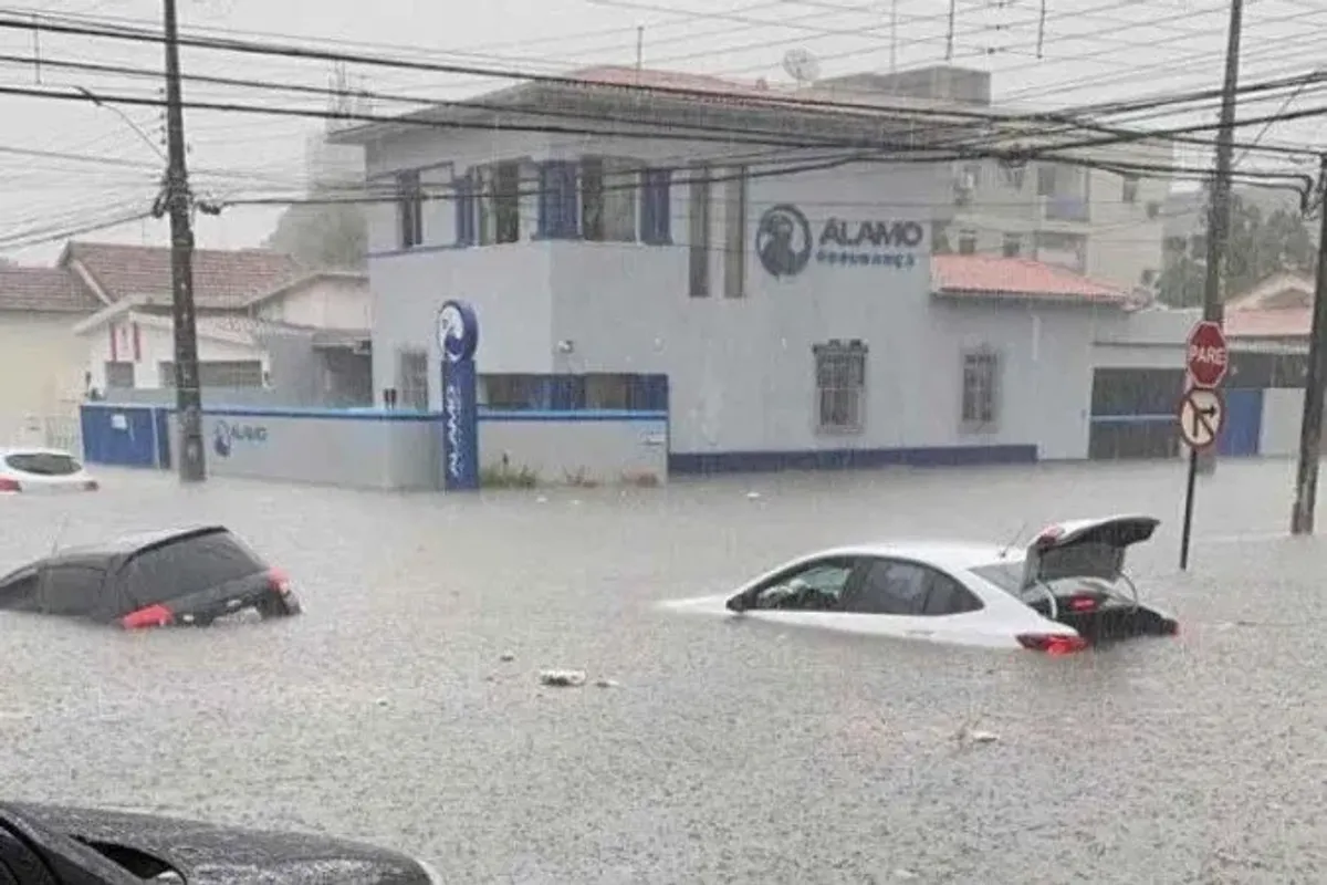 Rua alagada em cidade brasileira durante forte tempestade com chuva intensa e vento.