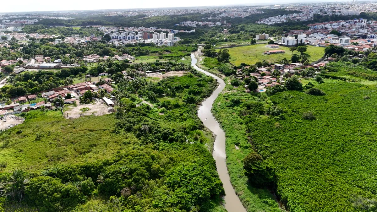 Rio urbano em João Pessoa com sinais de poluição e abandono, refletindo a realidade de comunidades próximas.