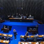 Senadores em corredor do Senado Federal, discutindo planos políticos para as eleições de 2026, com alguns visando governos estaduais e outros a reeleição.