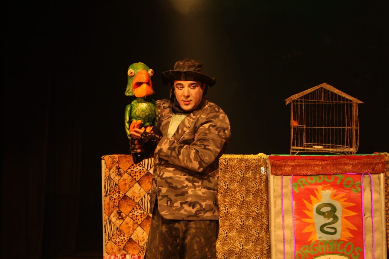Atores em performance teatral em festival nacional com público diverso assistindo em praça pública