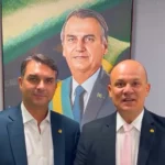 Flávio Bolsonaro discursando em um evento político do PL na Domus Hall em João Pessoa, com outros líderes do partido e uma multidão ao fundo.