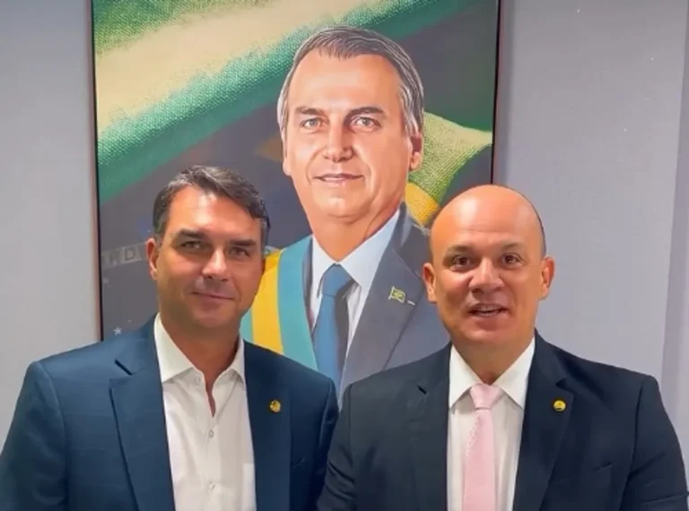 Flávio Bolsonaro discursando em um evento político do PL na Domus Hall em João Pessoa, com outros líderes do partido e uma multidão ao fundo.