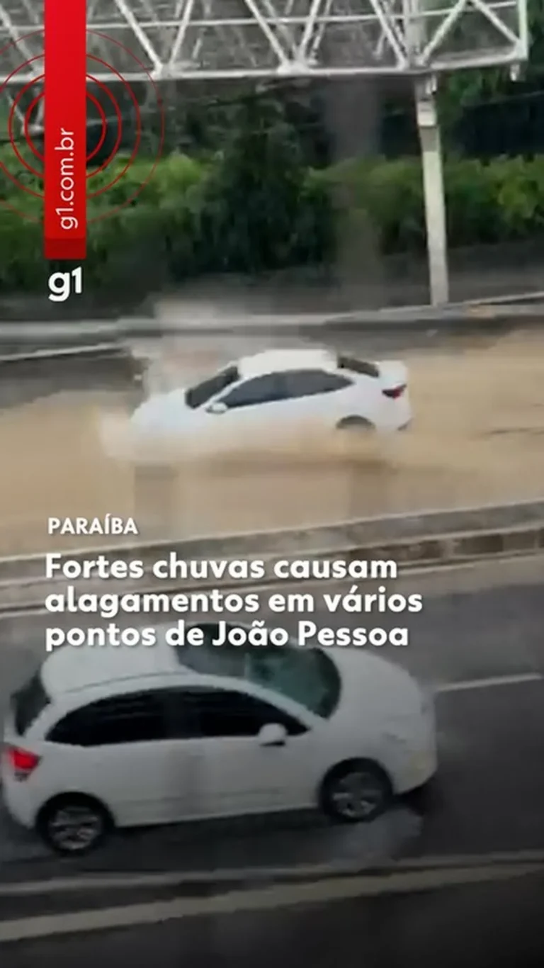 Rua alagada em João Pessoa após fortes chuvas, com tráfego de veículos.