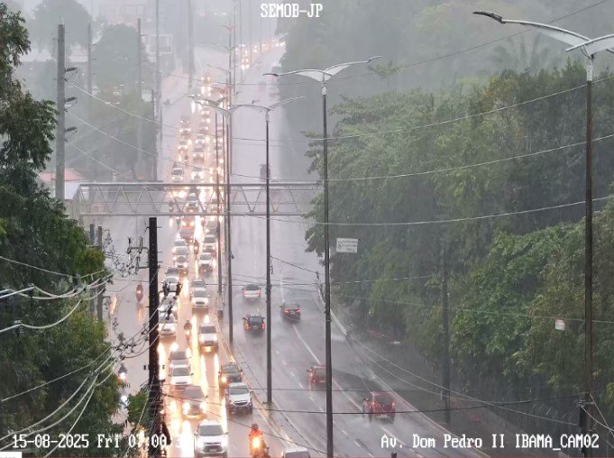 Rua alagada em João Pessoa durante chuva intensa com sinal da Defesa Civil em destaque.