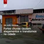 Avenida alagada em João Pessoa com carro parcialmente submerso devido a forte chuva.