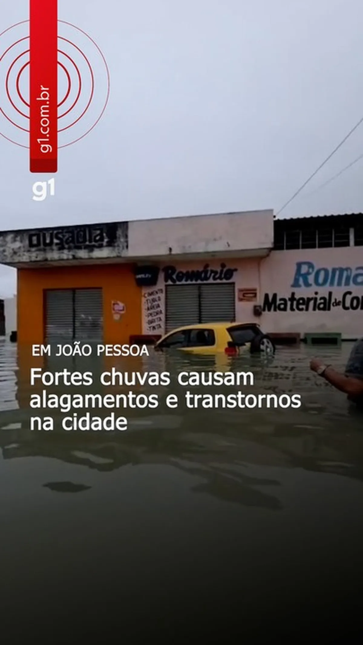 Avenida alagada em João Pessoa com carro parcialmente submerso devido a forte chuva.