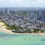Empreendimento imobiliário moderno em João Pessoa com vista para o mar ao pôr do sol.