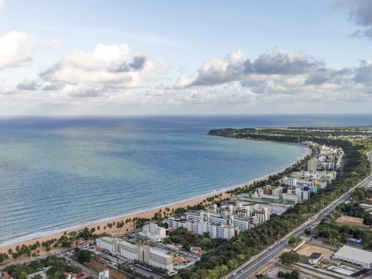 Skyline de João Pessoa ao pôr do sol, com edifícios modernos e guindastes de construção, simbolizando a valorização imobiliária e o desenvolvimento urbano da capital paraibana.