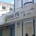 Candidatos em um escritório do Sine na Paraíba, preenchendo formulários e conversando com atendentes em busca de vagas de emprego.