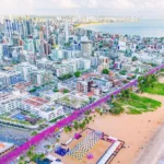 Corredores completando a Maratona de João Pessoa com público vibrando.