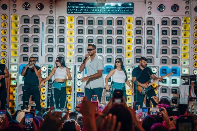Mikael Santos cantando em um palco iluminado do São João de Campina Grande, com a multidão ao fundo.