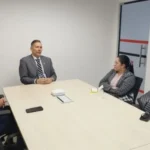 Dois homens em trajes formais, representando o Ministério Público e a Secretaria de Administração Penitenciária, apertando as mãos em um escritório, simbolizando colaboração.
