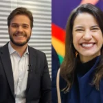 Multidão celebra em um arraial junino durante a noite, com barracas iluminadas e palco ao fundo.