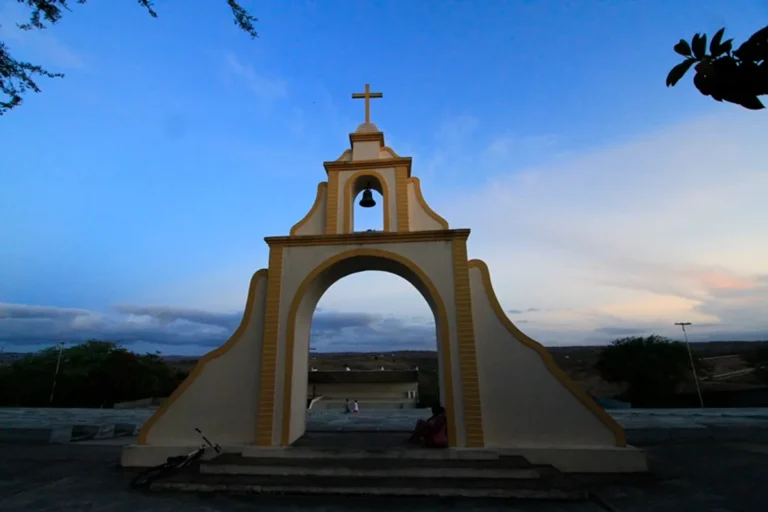Palco de festival em cidade histórica do interior da Paraíba durante o pôr do sol, com público reunido.