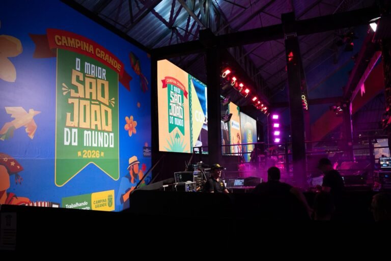 Multidão celebrando durante o São João em Campina Grande, com barracas típicas e palco ao fundo.