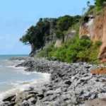 Barreira do Cabo Branco em João Pessoa apresentando sinais de erosão e risco de deslizamento, com fita de isolamento.