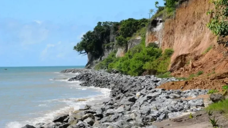 Barreira do Cabo Branco em João Pessoa apresentando sinais de erosão e risco de deslizamento, com fita de isolamento.