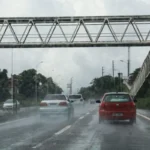 Rua em João Pessoa sob forte chuva e ventos intensos com galhos de árvores caindo e pessoas buscando abrigo.