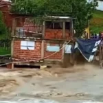 Rua inundada em cidade da Paraíba após chuvas fortes, com moradores em barcos e casas alagadas.
