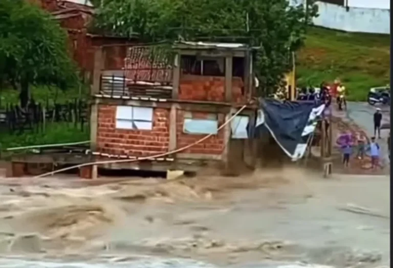 Rua inundada em cidade da Paraíba após chuvas fortes, com moradores em barcos e casas alagadas.