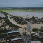 Rua alagada com casas submersas devido a fortes chuvas em Pernambuco ou Paraíba, com equipes de resgate em ação.