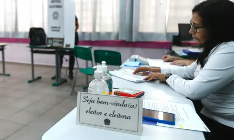 Mesário sorridente auxilia eleitores em seção de votação