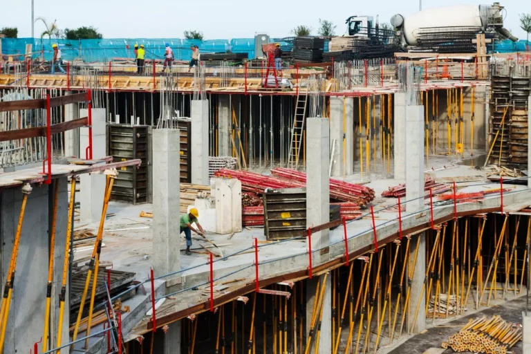 Trabalhadores em um canteiro de obras em João Pessoa, com edifícios modernos ao fundo.
