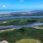 Expansão urbana na Grande João Pessoa com construções próximas ao estuário do Rio Paraíba e manguezais.