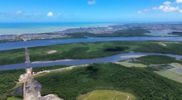 Expansão urbana na Grande João Pessoa com construções próximas ao estuário do Rio Paraíba e manguezais.