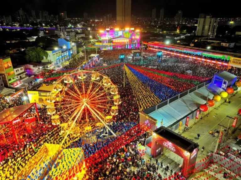 Multidão celebra as festas de São João em Campina Grande, Paraíba, com palco iluminado e bandeirinhas coloridas ao fundo.