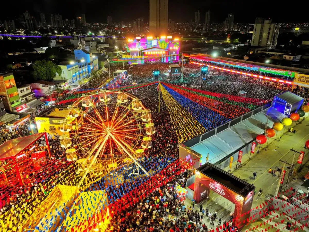 Multidão celebra as festas de São João em Campina Grande, Paraíba, com palco iluminado e bandeirinhas coloridas ao fundo.