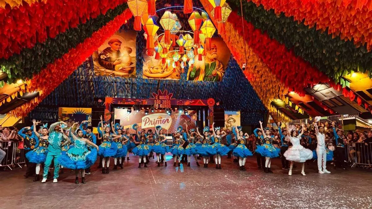 Pessoas dançando quadrilha com bandeirinhas e fogueira em uma festa junina vibrante na Paraíba