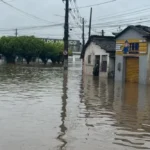 Ruas de João Pessoa inundadas após fortes chuvas, com carros parcialmente submersos.
