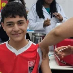 Enfermeira vacinando adolescente em escola de João Pessoa