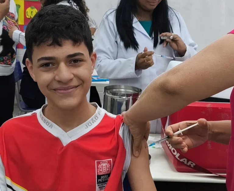 Enfermeira vacinando adolescente em escola de João Pessoa