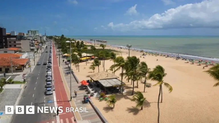 Orla de João Pessoa ao pôr do sol, com prédios modernos e praia movimentada.