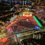 Multidão celebra em frente à entrada do Parque do Povo em Campina Grande, com câmeras de segurança visíveis e iluminação festiva.