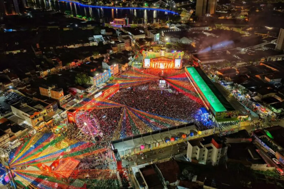 Multidão celebra em frente à entrada do Parque do Povo em Campina Grande, com câmeras de segurança visíveis e iluminação festiva.