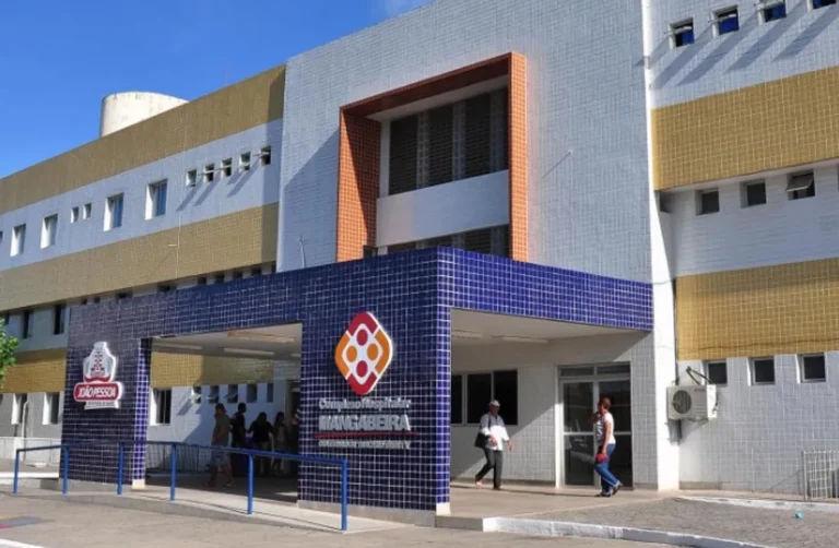 Entrada de um hospital em João Pessoa durante a noite, com ambulância ao fundo.