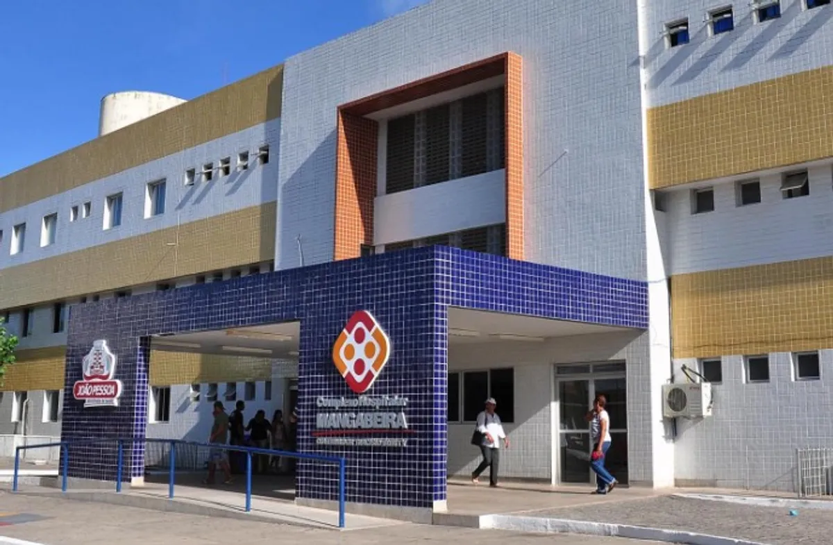 Entrada de um hospital em João Pessoa durante a noite, com ambulância ao fundo.