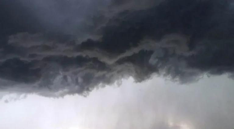 Rua de João Pessoa sob chuva intensa com ventos fortes, pessoas com guarda-chuvas e reflexos de luzes no chão molhado durante alerta do Inmet na Paraíba.