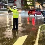Rua inundada em cidade da Paraíba após chuvas intensas, com pessoas desabrigadas e carros submersos.