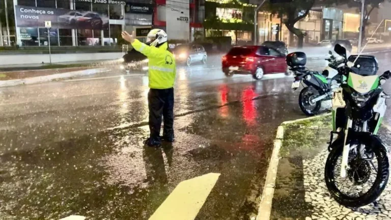 Rua inundada em cidade da Paraíba após chuvas intensas, com pessoas desabrigadas e carros submersos.